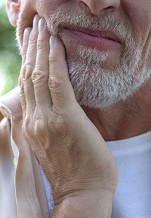 Man rubbing his jaw in pain with trees in background