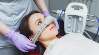 A dentist placing an inhalation nose mask on a woman