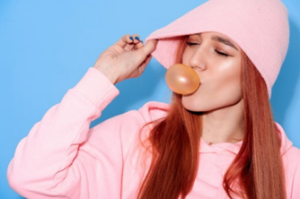 Woman in pink hoodie blowing a bubblegum bubble